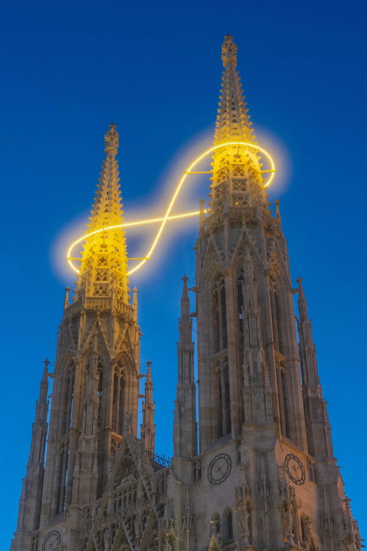 Billi Thanner Lichtinstallation Votivkirche Wien - leuchtende Unendlichkeitsschleife zwischen den Türmen bei blauer Stunde