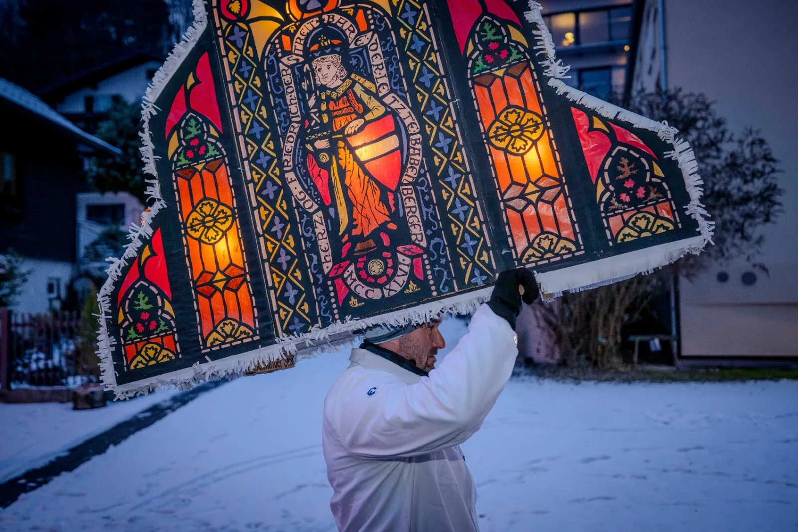 Glöckler trägt gotische Fensterkappe mit Heiligenfigur bei Dämmerung im Schnee