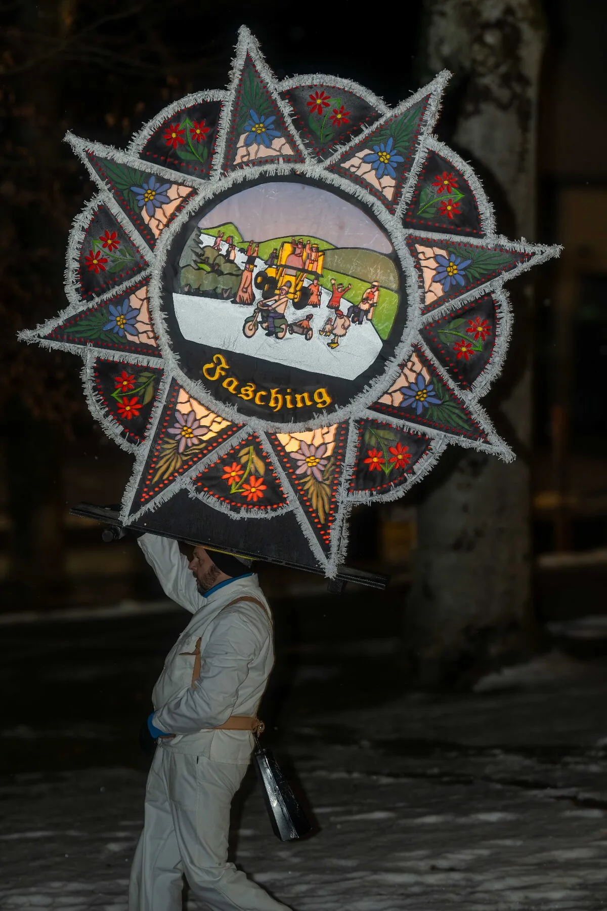 Glöckler mit Fasching-Kappe zeigt ländliche Szene mit Alpen