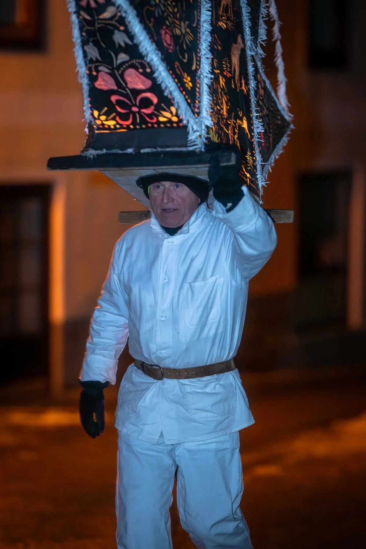 Glöckler in weißer Tracht mit floraler Laternenkappe im Abendlicht