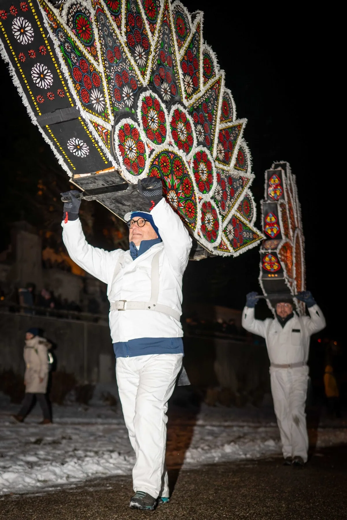 Zwei Glöckler mit großen Rosettenkappen und Blumenmotiven bei Nacht