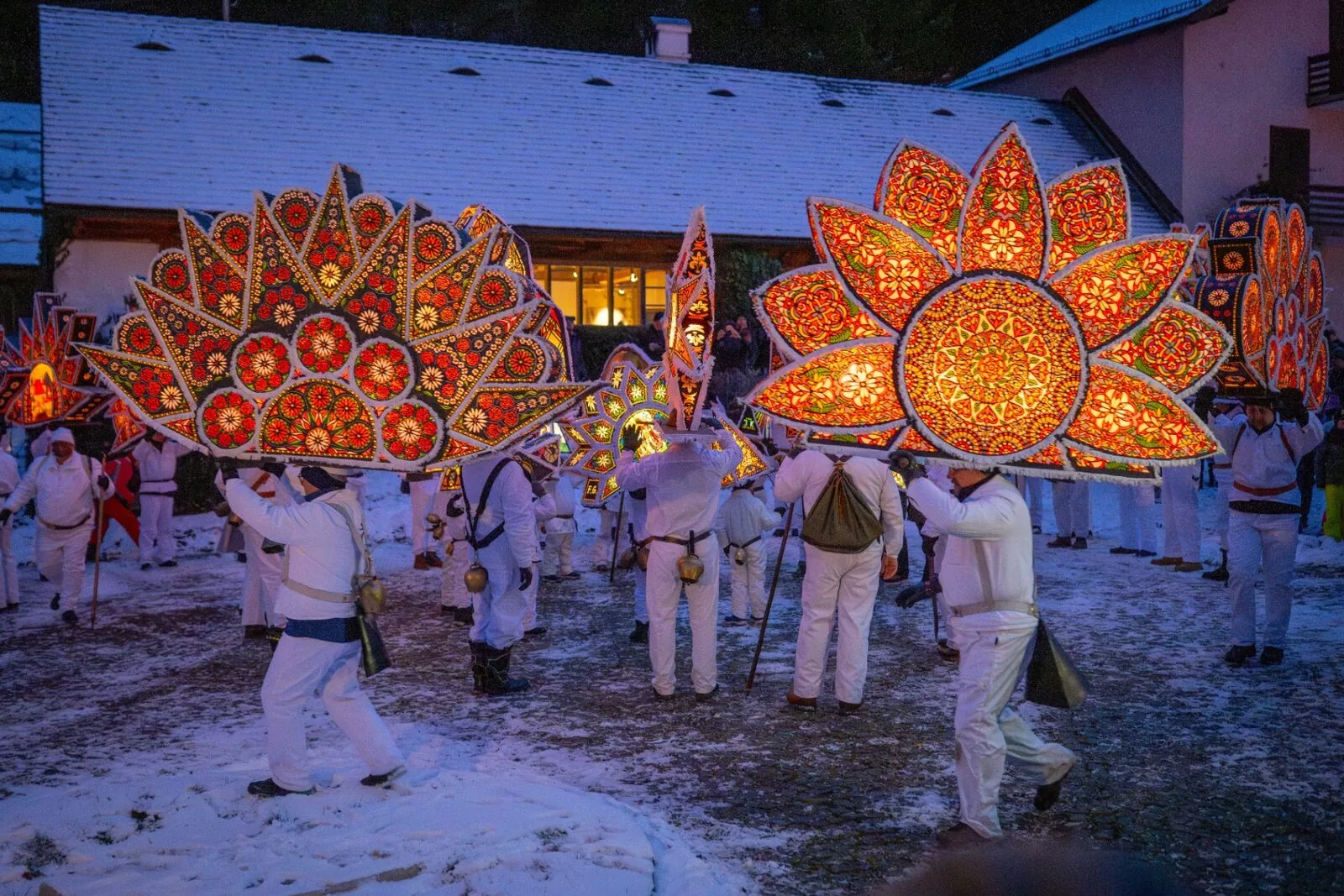 Zwei große Glöcklerkappen mit Blumenmotiven und Zuschauer im Hintergrund bei Nacht
