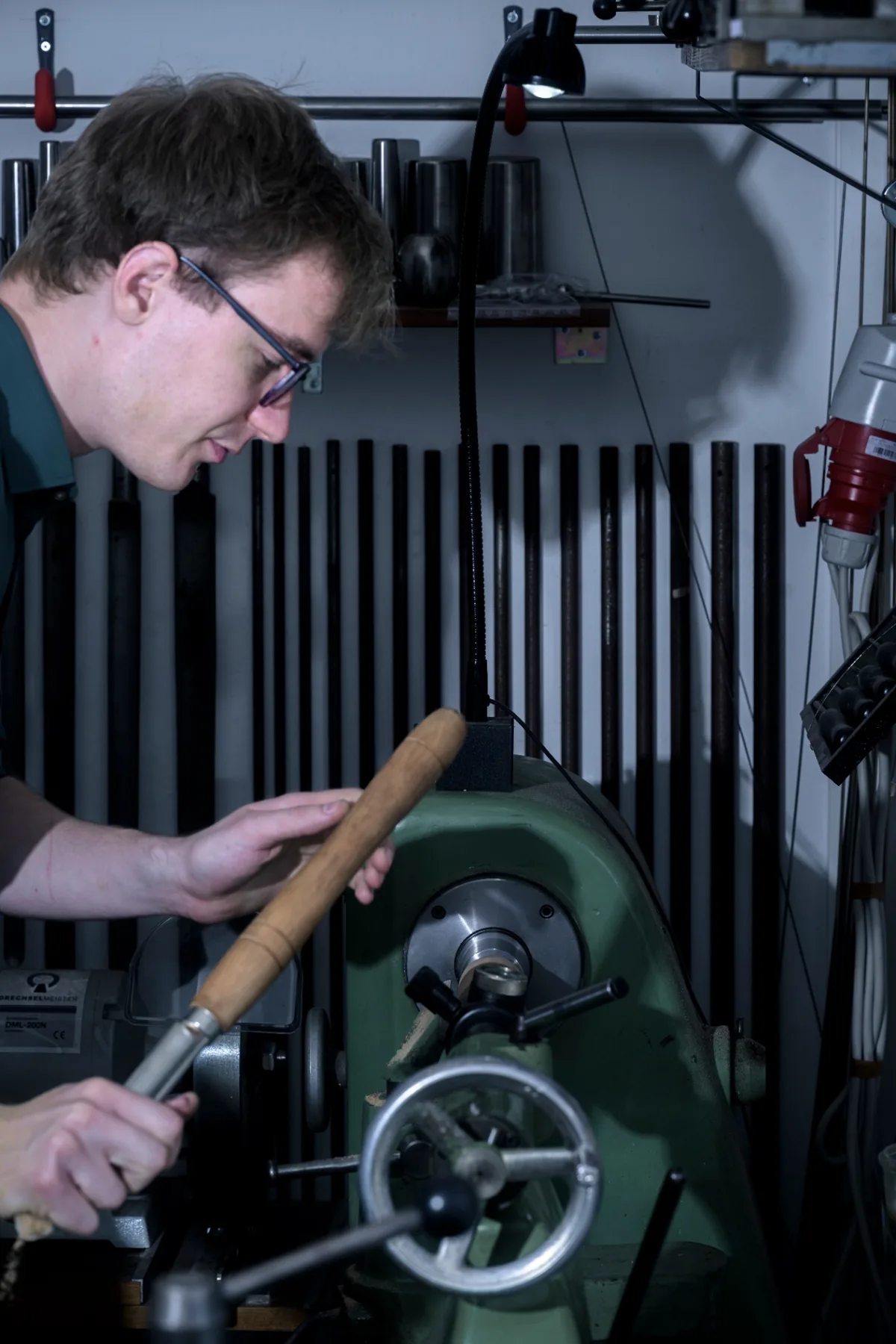 Florian Köck concentrated at the wood lathe, turning a wooden component under focused light in his Vienna workshop.