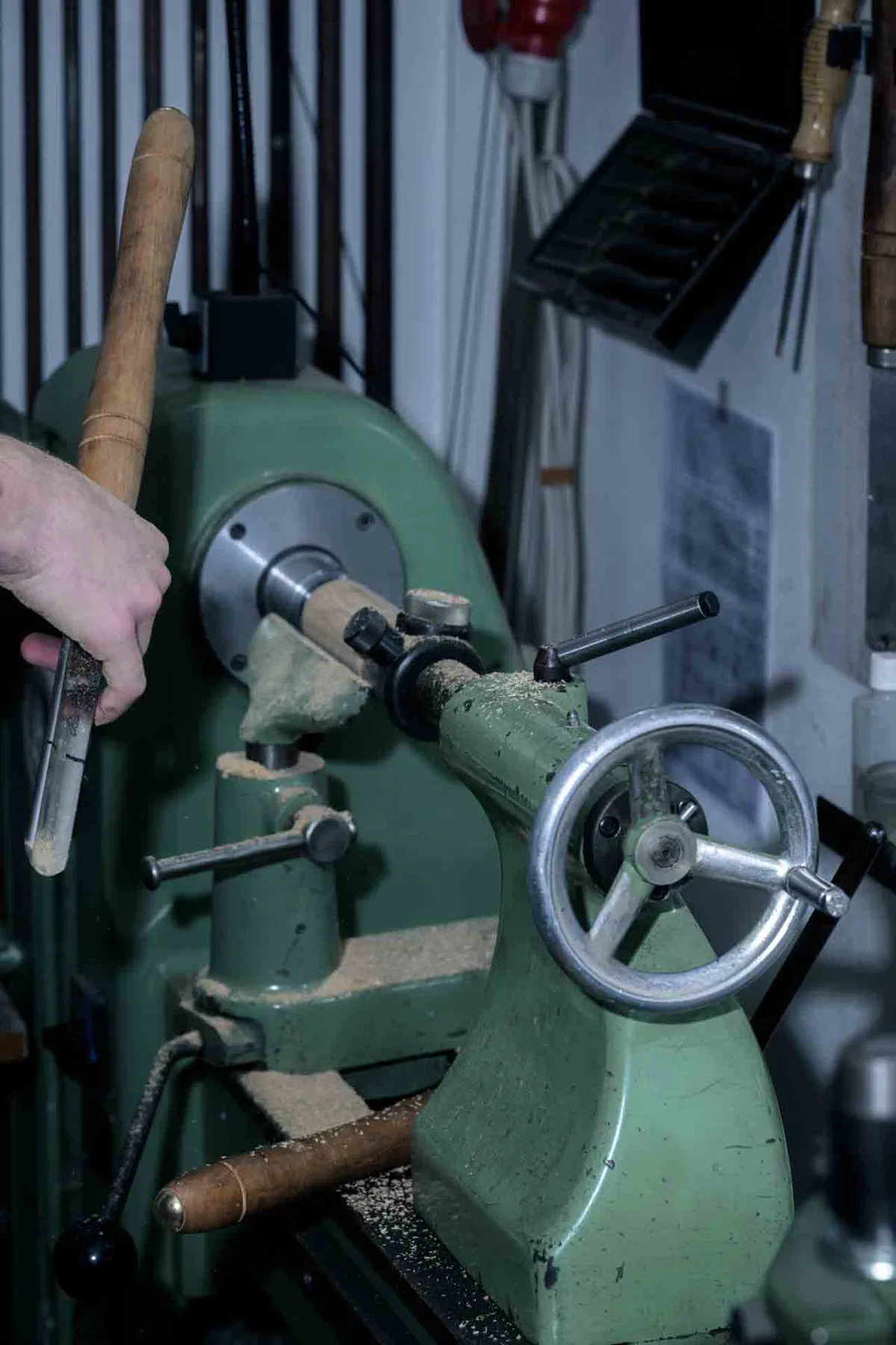 A hand guiding a wooden dowel on the lathe in Florian Köck's workshop, sawdust gathering on the machine bed.