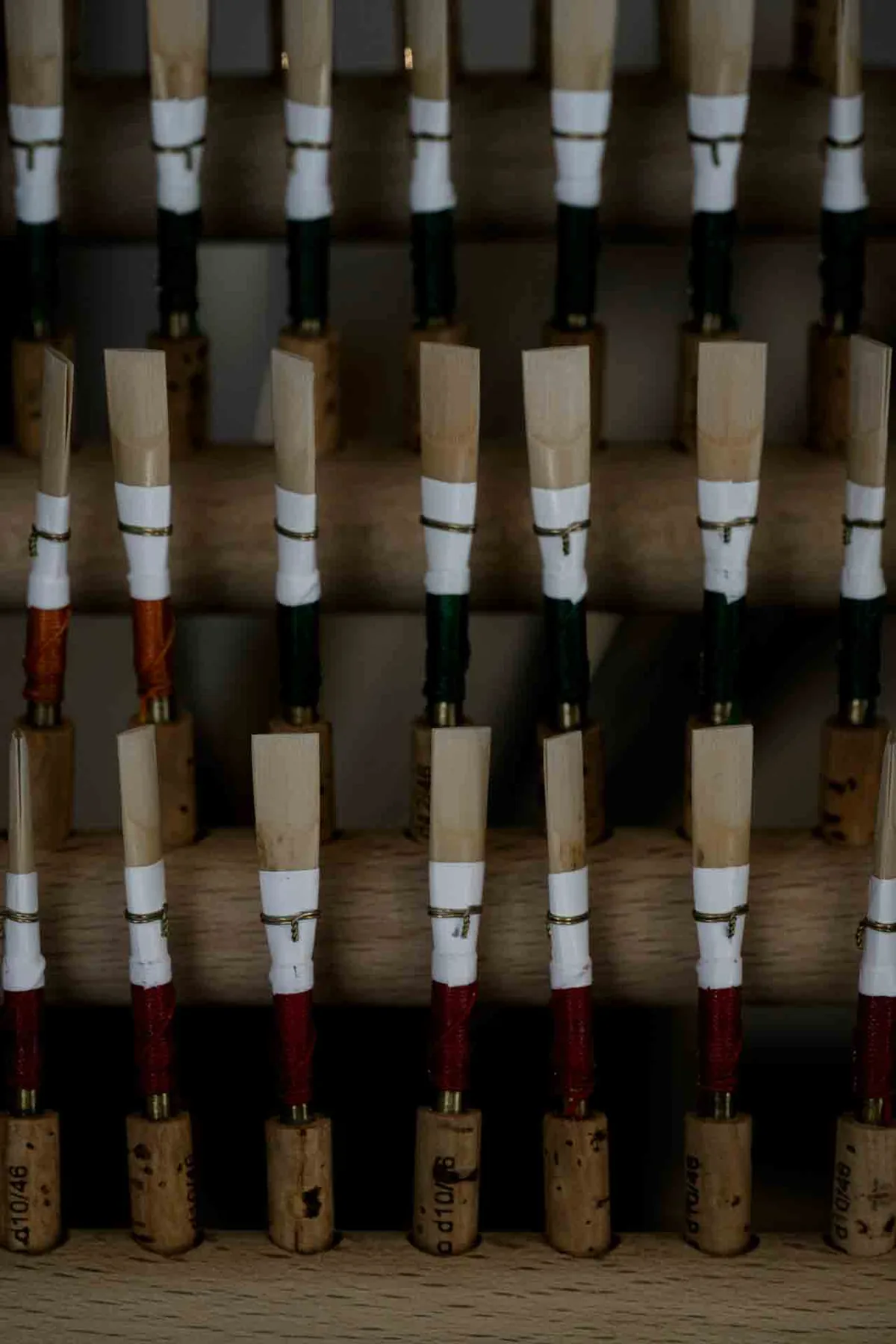 Rows of handmade oboe reeds bound with coloured thread, arranged on a wooden rack — quiet evidence of experience and tradition.