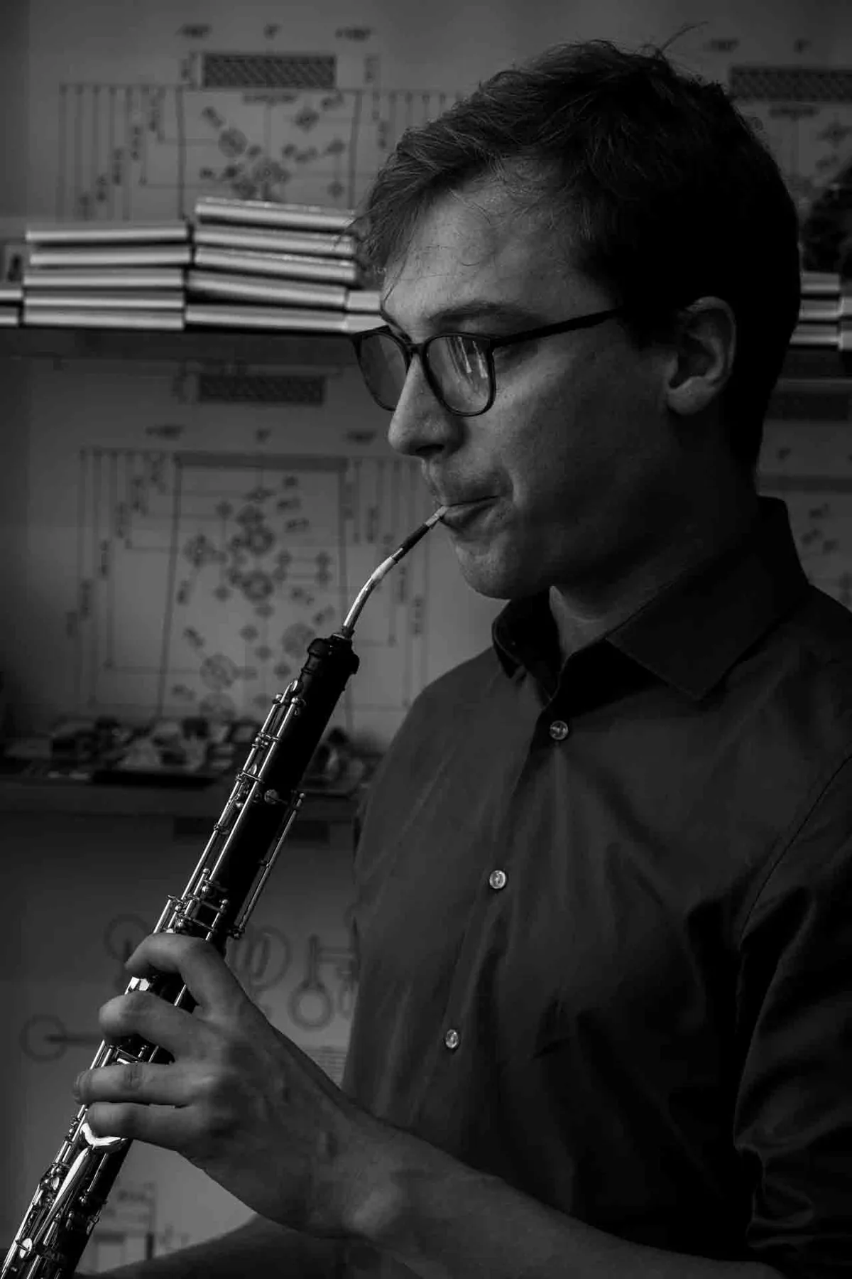 Black-and-white portrait of Florian Köck playing the oboe in front of technical fingering charts — the maker returning to the musician.
