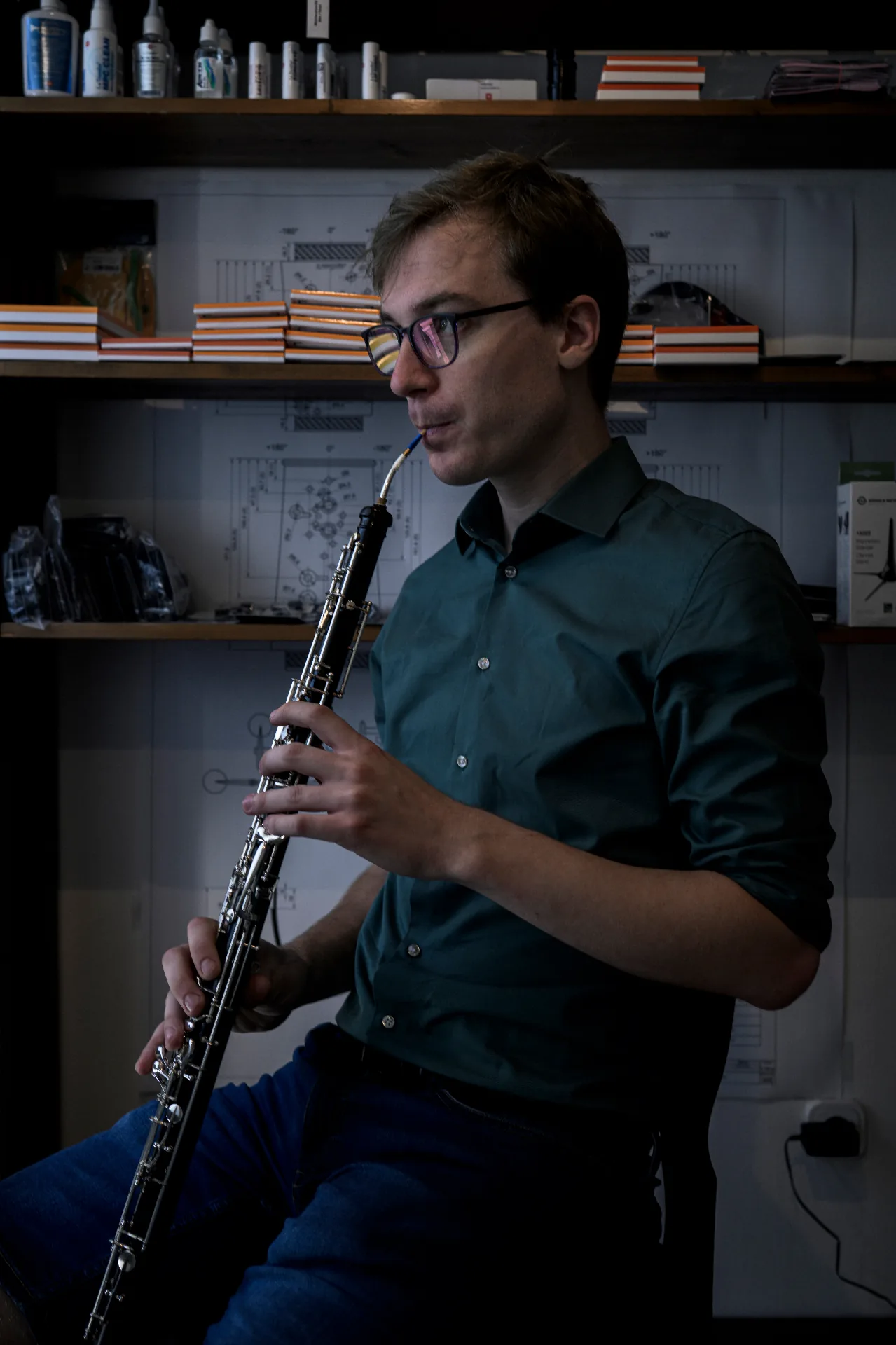 Florian Köck seated in his Vienna workshop, playing the oboe in front of technical drawings — the emotional key image of the story.