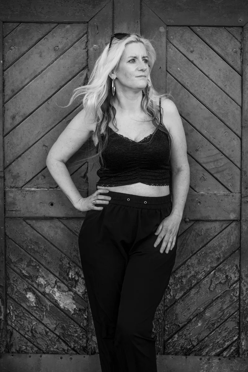Standing portrait at rustic chevron wooden door — confident pose, full body black and white fine art