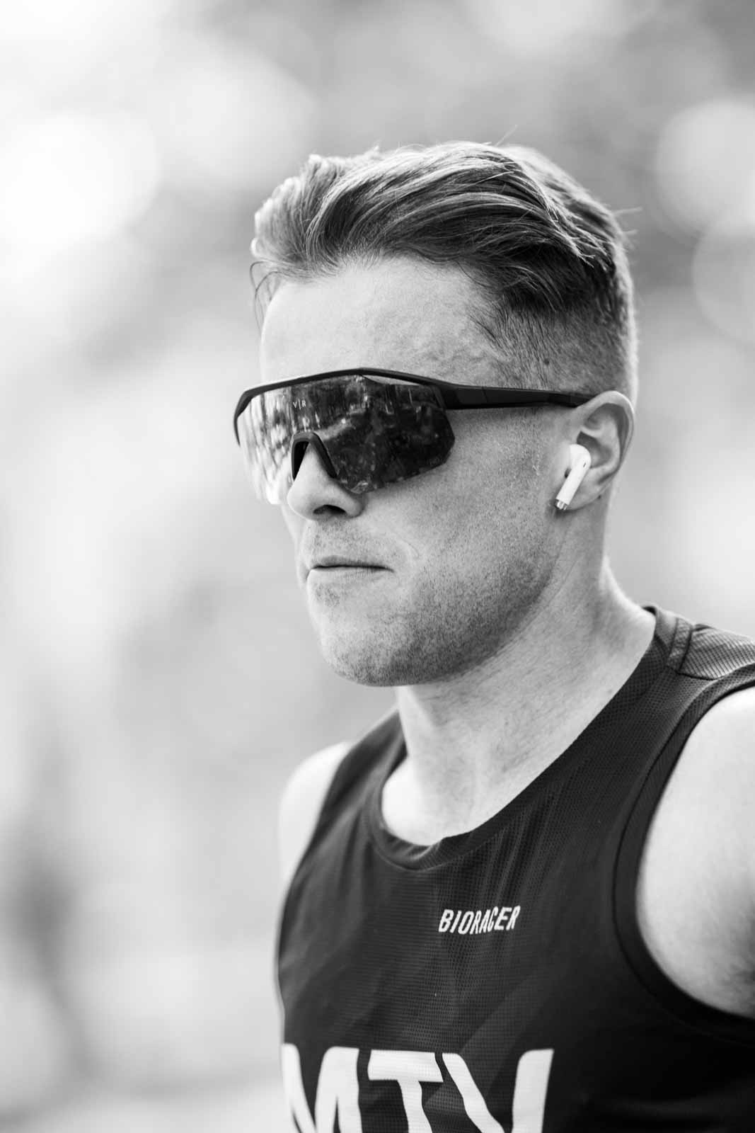 Focused marathon runner with sleek hair and sport sunglasses — black and white portrait photography by schopho