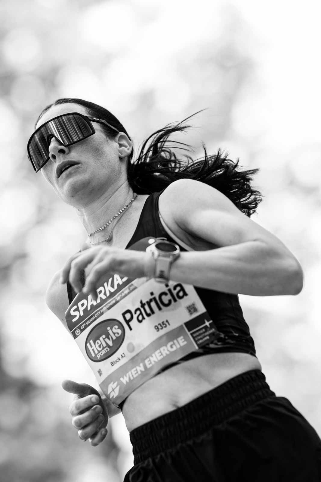 Dynamic low-angle portrait of marathon runner Patricia checking her watch — black and white editorial photography by Peter Scholz