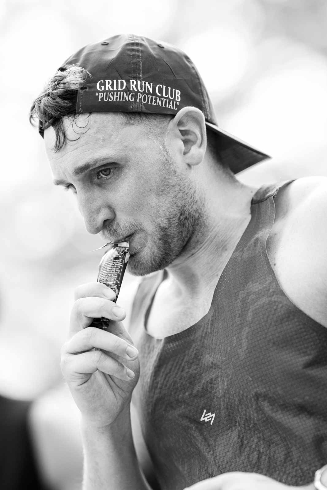 Marathon runner with Grid Run Club cap taking an energy gel at the Vienna City Marathon — black and white fine art portrait photography by Peter Scholz, schopho