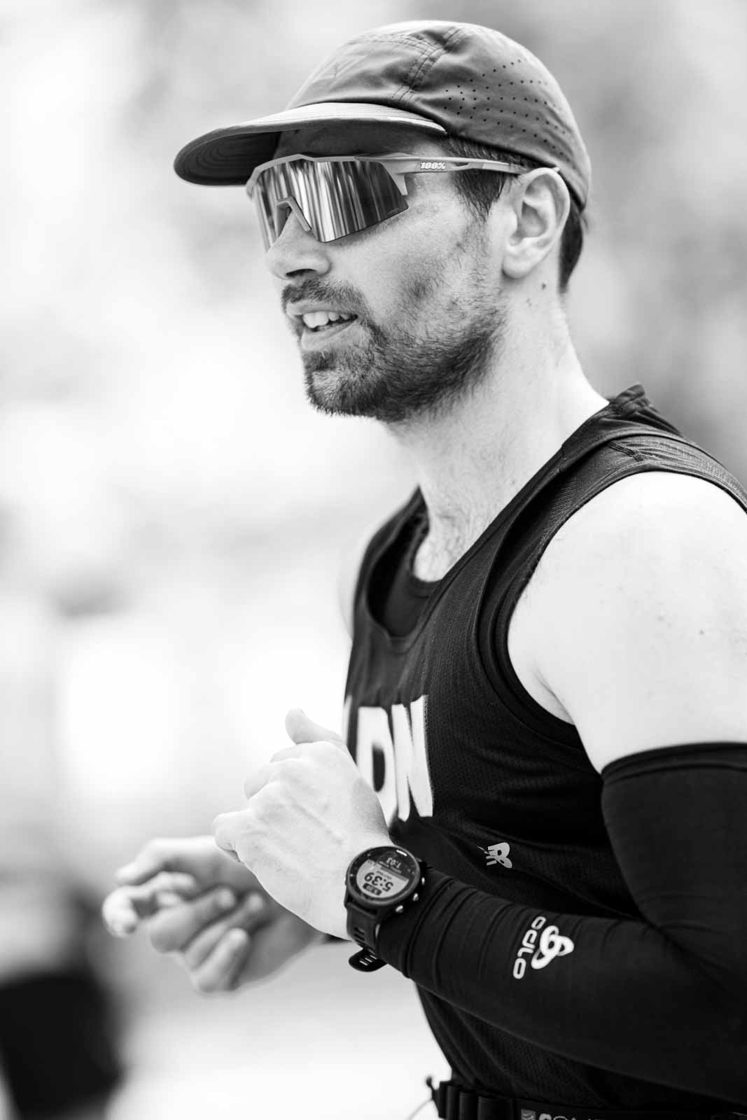 Marathon runner with cap and mirrored sport sunglasses checking his watch — black and white portrait photography by Peter Scholz