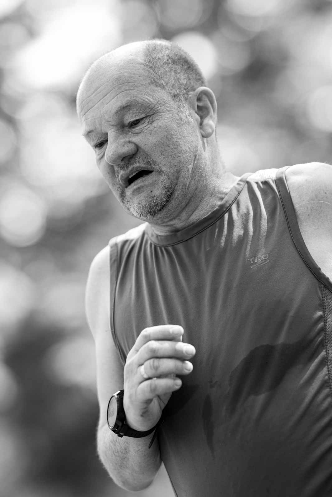 Intimate portrait of a senior marathon runner with TAO singlet at kilometer 35 — black and white fine art photography by schopho