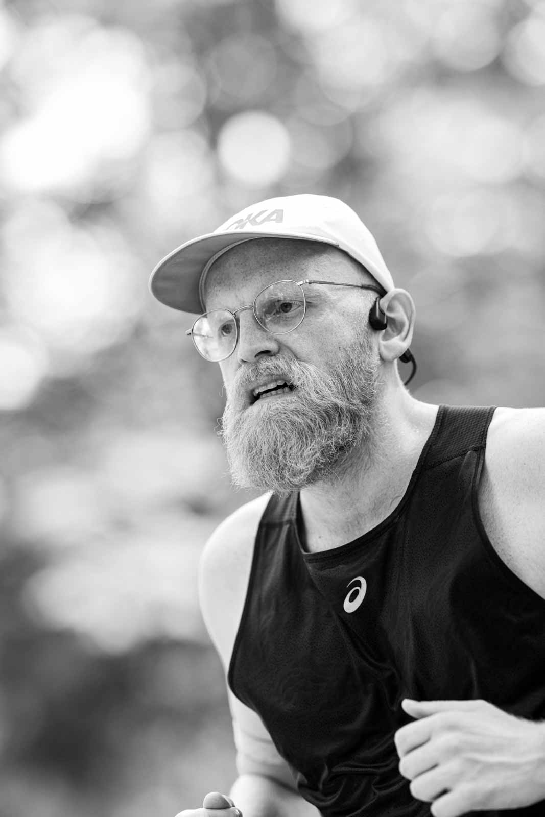 Marathon runner with grey beard, round glasses and Hoka cap at the Vienna City Marathon — black and white fine art photography by Peter Scholz