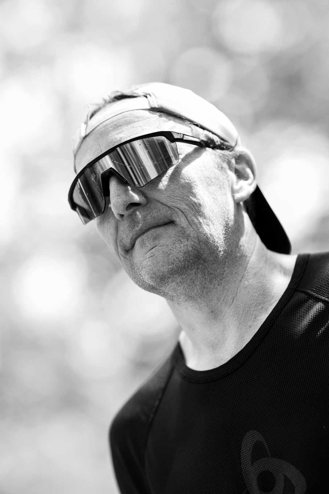 Marathon runner with cap and mirrored sport sunglasses, intense low-angle portrait — black and white fine art photography by schopho
