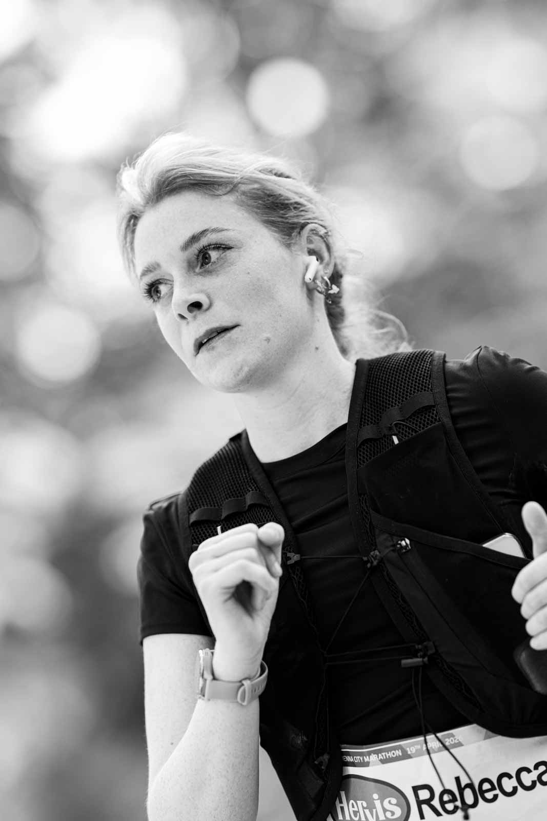 Female marathon runner Rebecca with hydration vest and AirPods at the Vienna City Marathon — black and white portrait photography by Peter Scholz