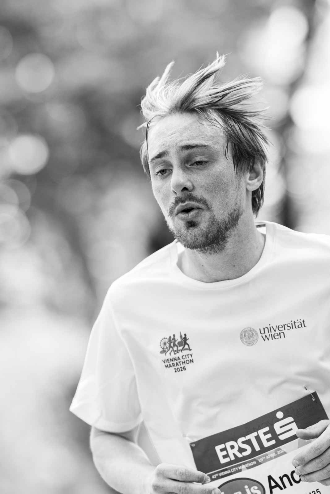 Marathon runner André with windblown hair and Vienna City Marathon 2026 shirt from Universität Wien — black and white portrait photography by schopho