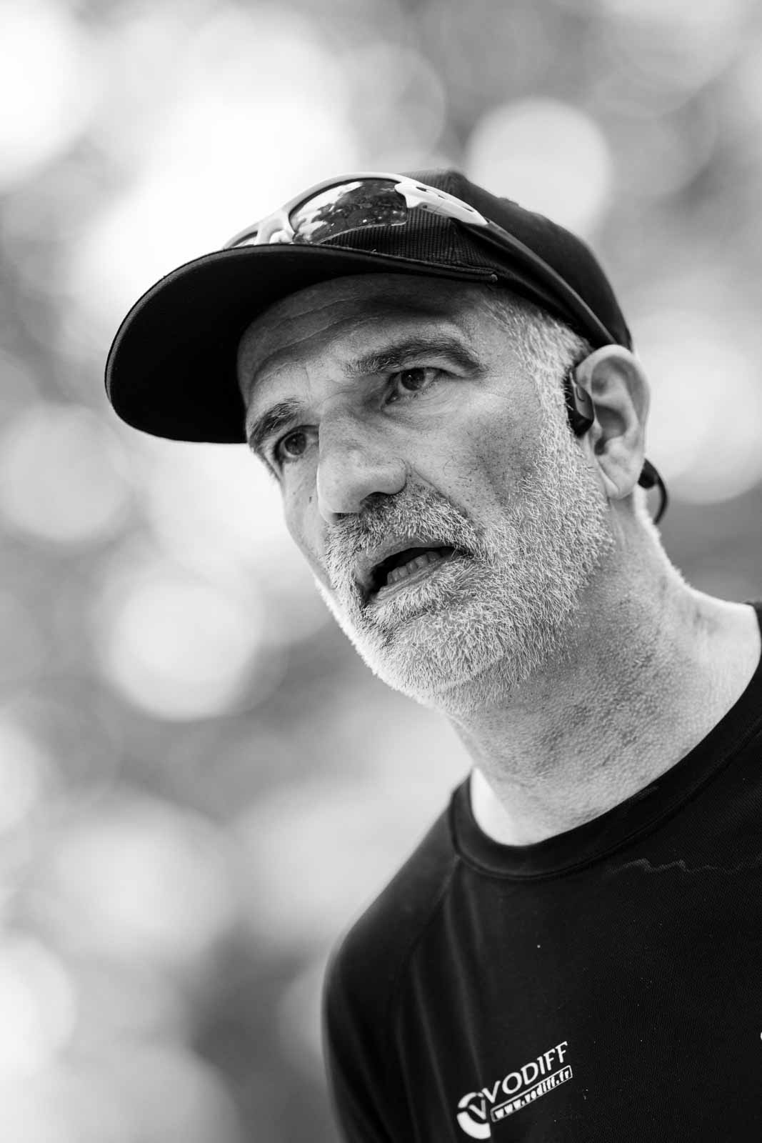 Senior marathon runner with Vodiff cap and bone-conduction headphones — black and white portrait photography by schopho