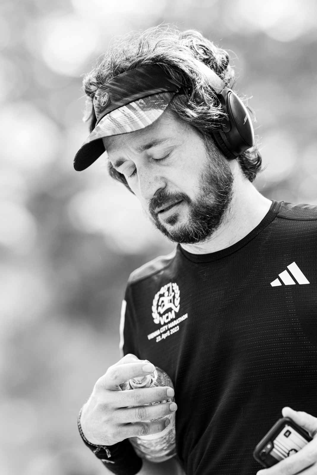 Marathon runner with Buff visor, Bose headphones and VCM 2023 shirt — black and white portrait photography by Peter Scholz