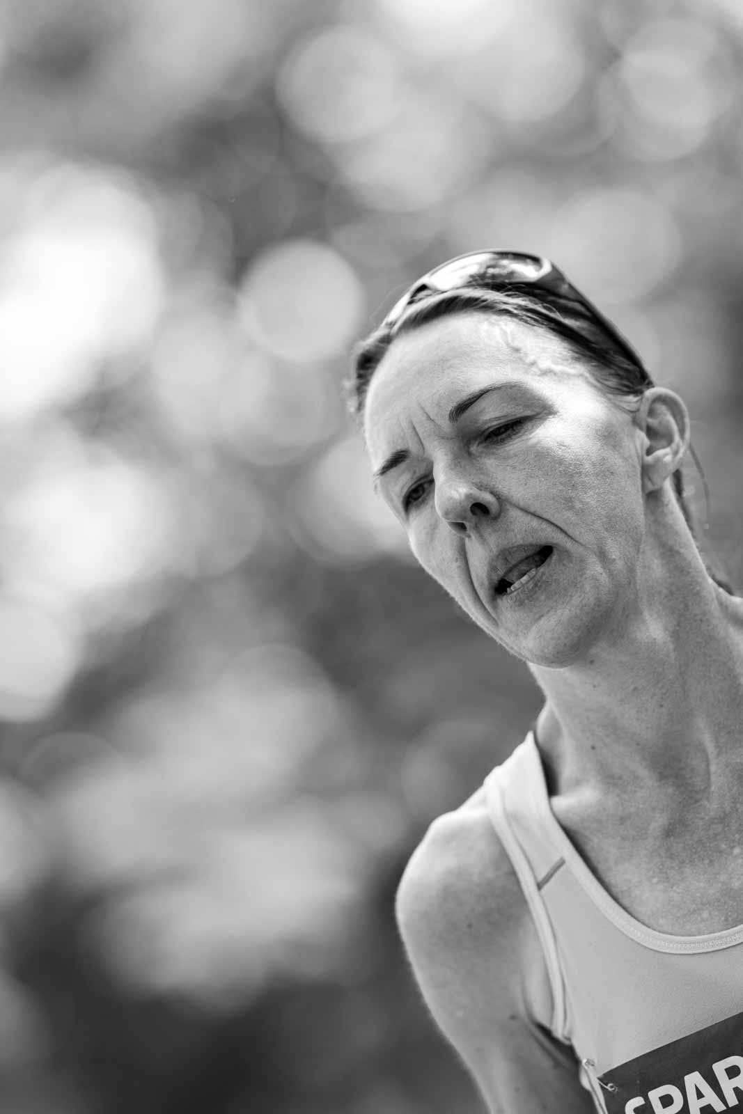 Female marathon runner with sport sunglasses on her head, intense expression at kilometer 35 — black and white fine art photography by schopho